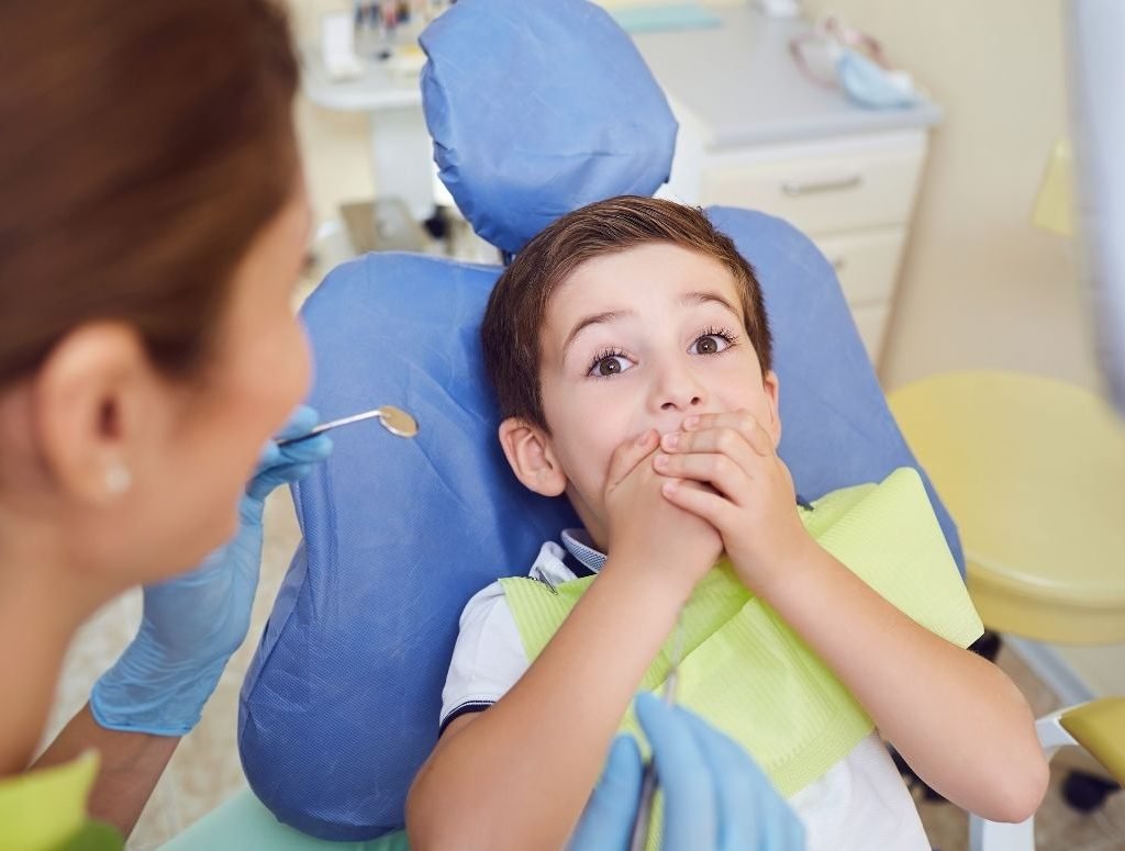Image of a young boy covering his mouth as a dental professional attempts to do an oral inspection