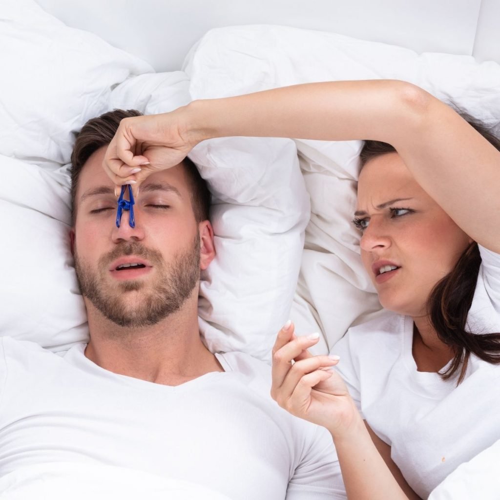 Main image of the "anti-snoring" page where shown is a couple in bed - the lady is pinching the man's nose with a clothespin because he is snoring too loudly