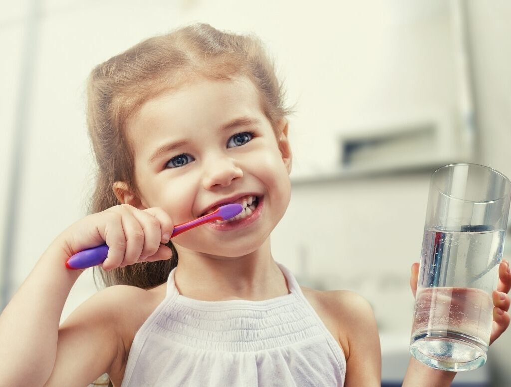 Image of a young girl brushing her teeth and holding a glass of water