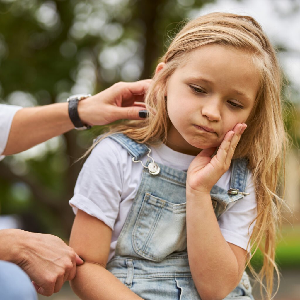 Image of a little girl outdoors holding her teeth, presumably after getting her teeth hurt