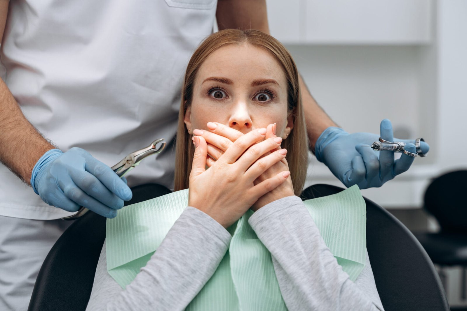 Image of a lady who looks scared covering her mouth with both hands at the clinic while a dental practitioner is behind her