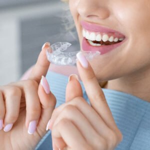 Image of a lady holding clear braces next to her teeth while smiling